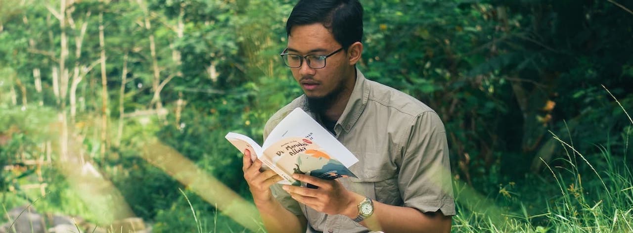 young guy reading a paperback in the forest