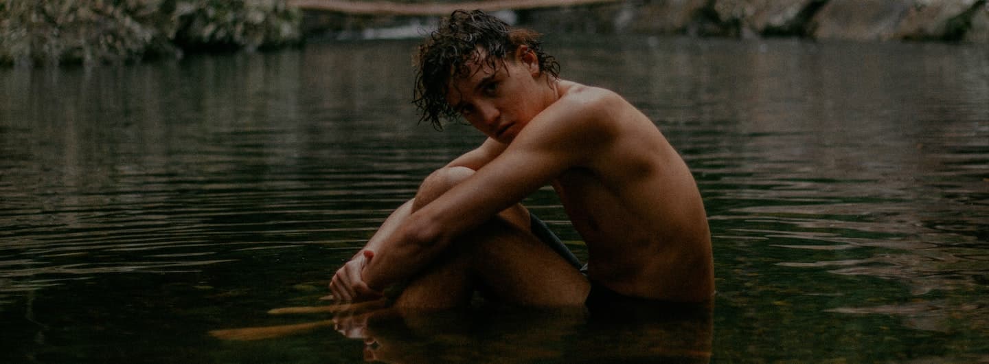 young guy sitting in a lake dark
