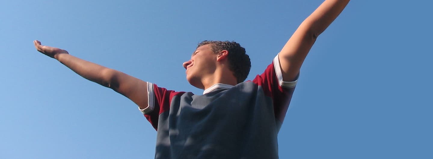 young guy with hands up against a blue sky