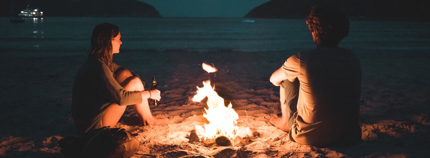 couple sitting by a campfire on a beach